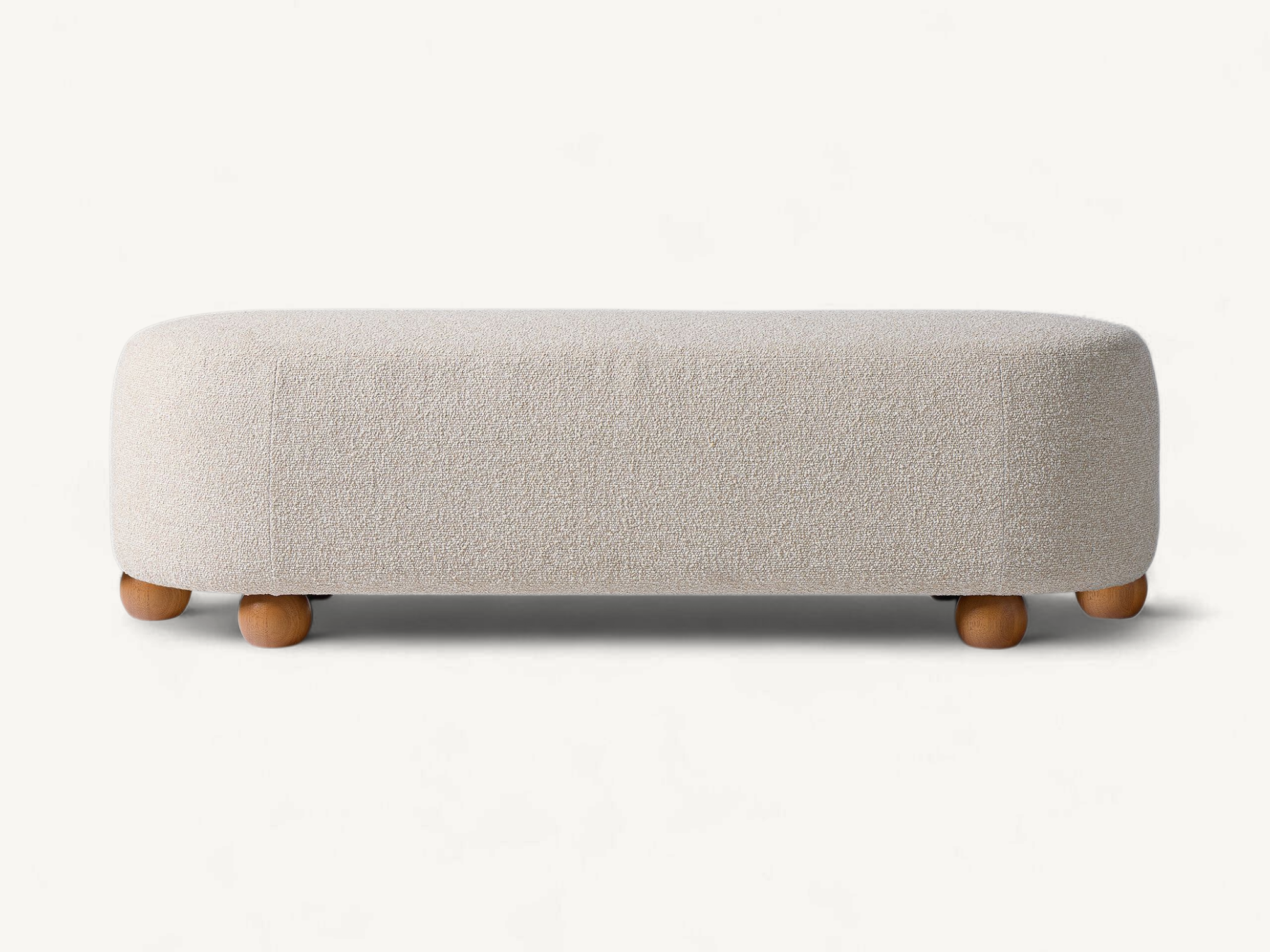 Upholstered long bench with rounded edges and solid teak wood spherical legs in a neutral cream fabric.