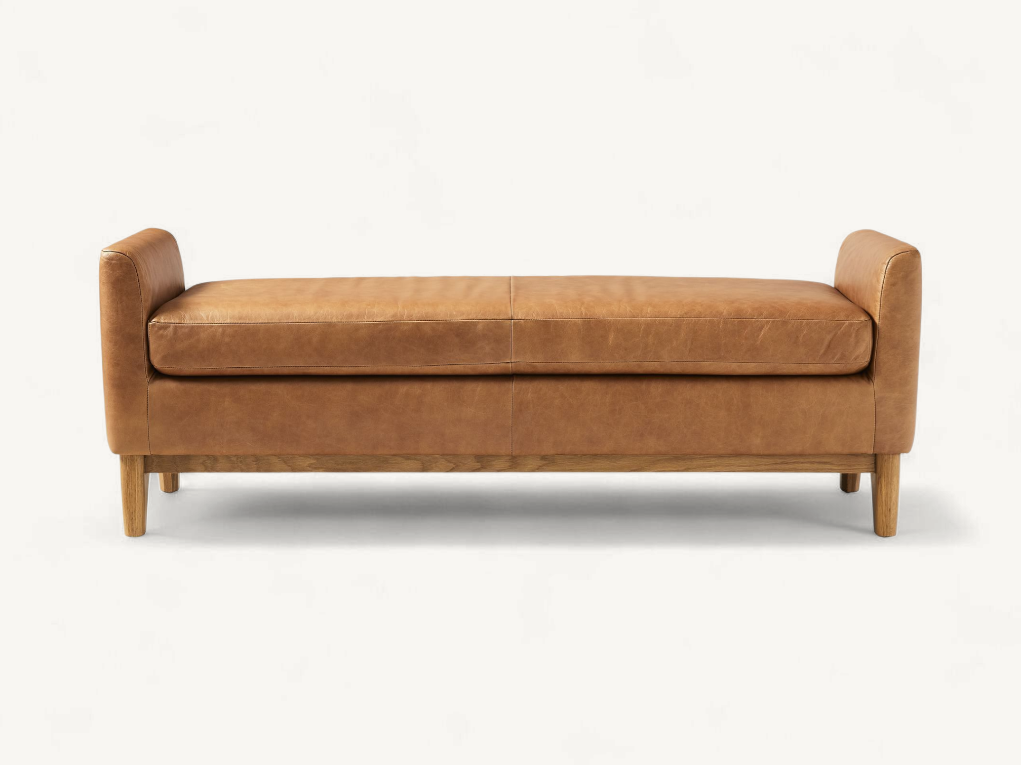Elegant tan leather upholstered bench with side bolsters and tapered solid teak wood legs on a white background.