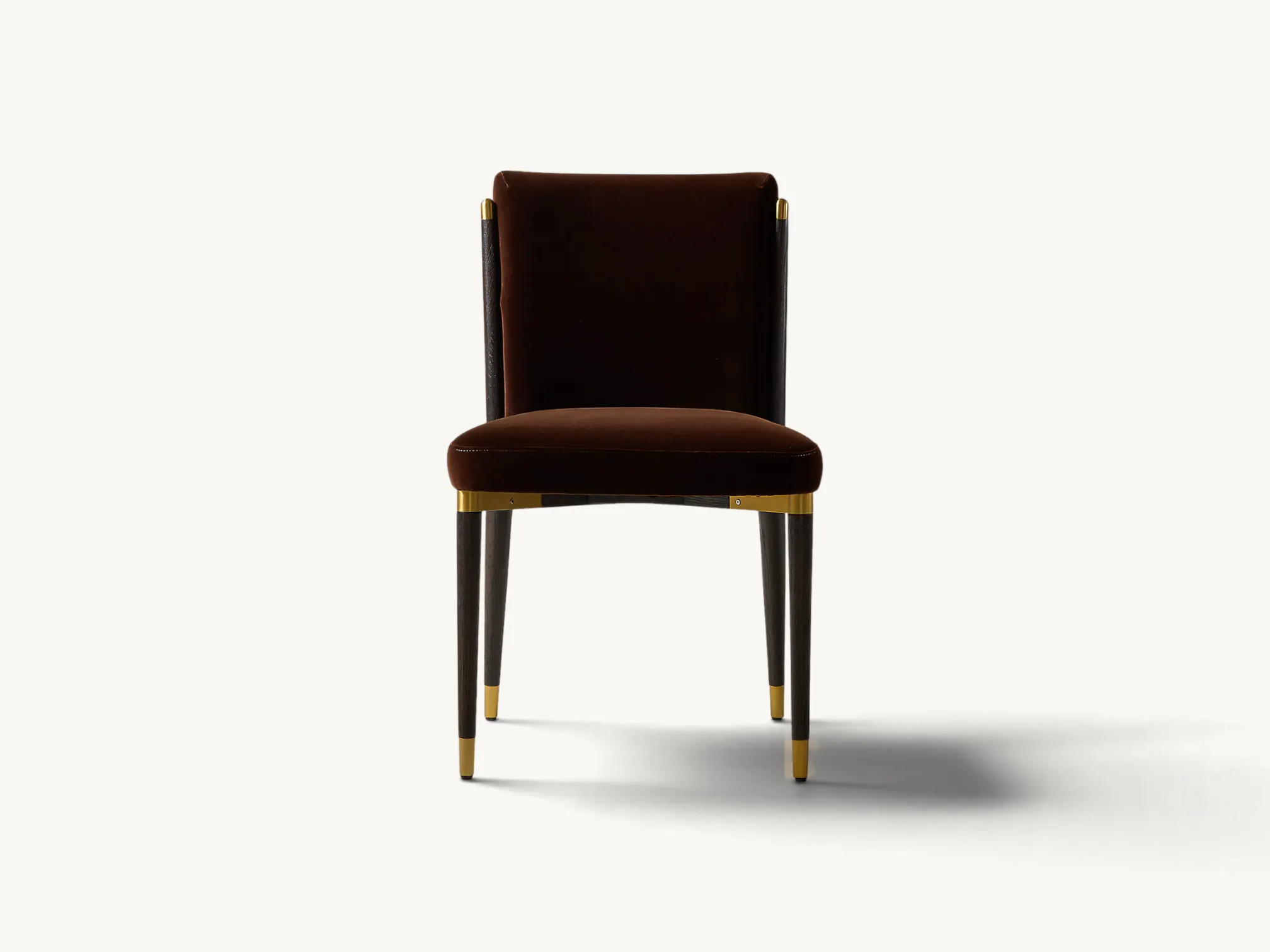 Armless dining chair upholstered in dark brown velvet with tapered dark wooden legs and brass metal accents