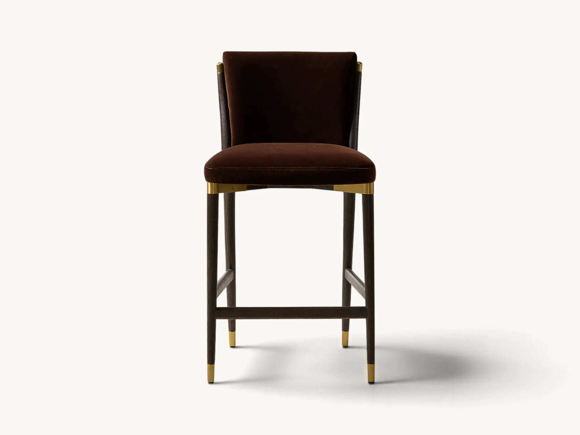 Upholstered wooden counter stool in dark brown velvet with tapered dark legs and brass metal accents